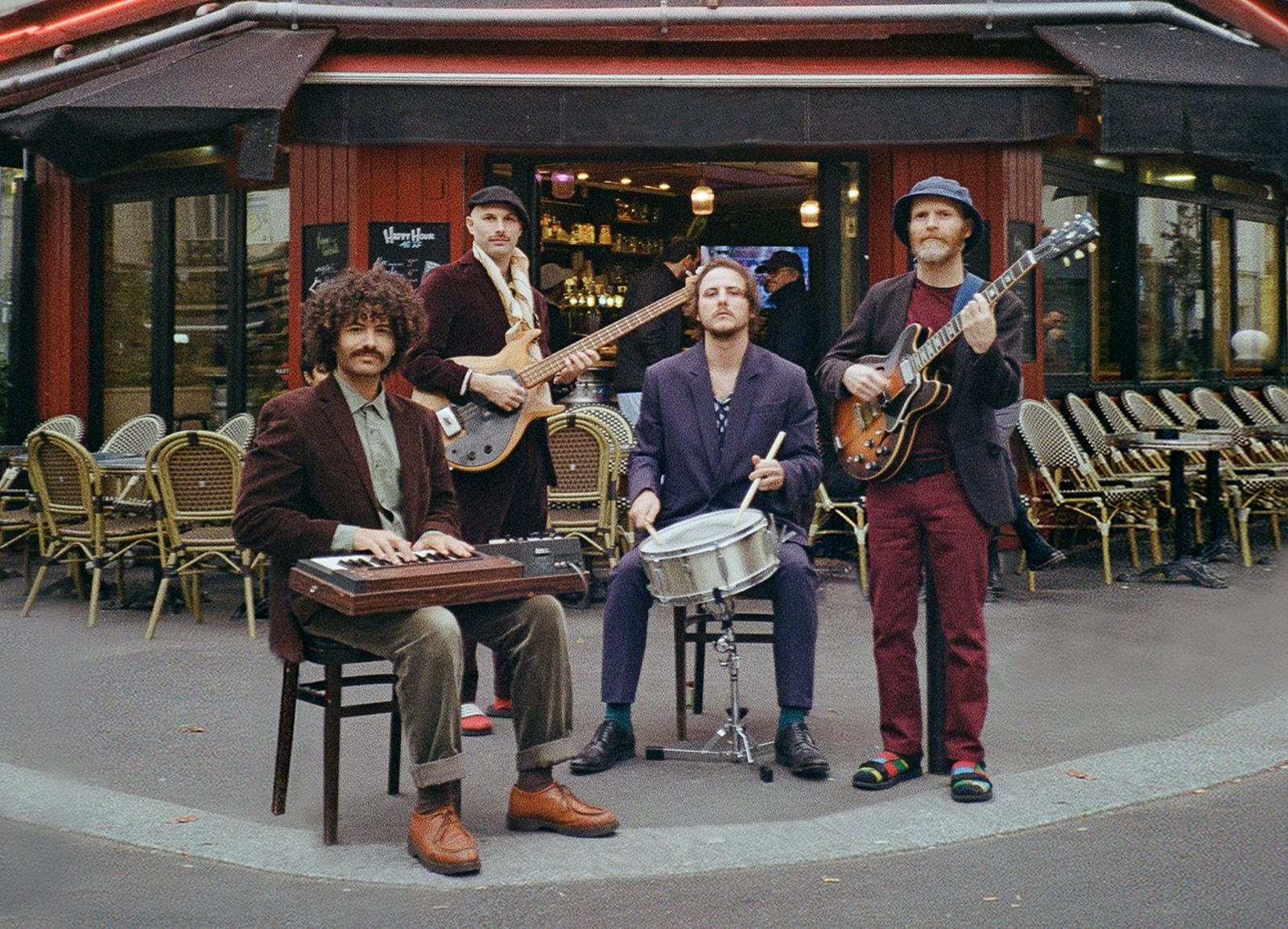 Eine vierköpfige Band spielt am Straßenrand vor einem Café, Keyboard, Gitarren und Snare.